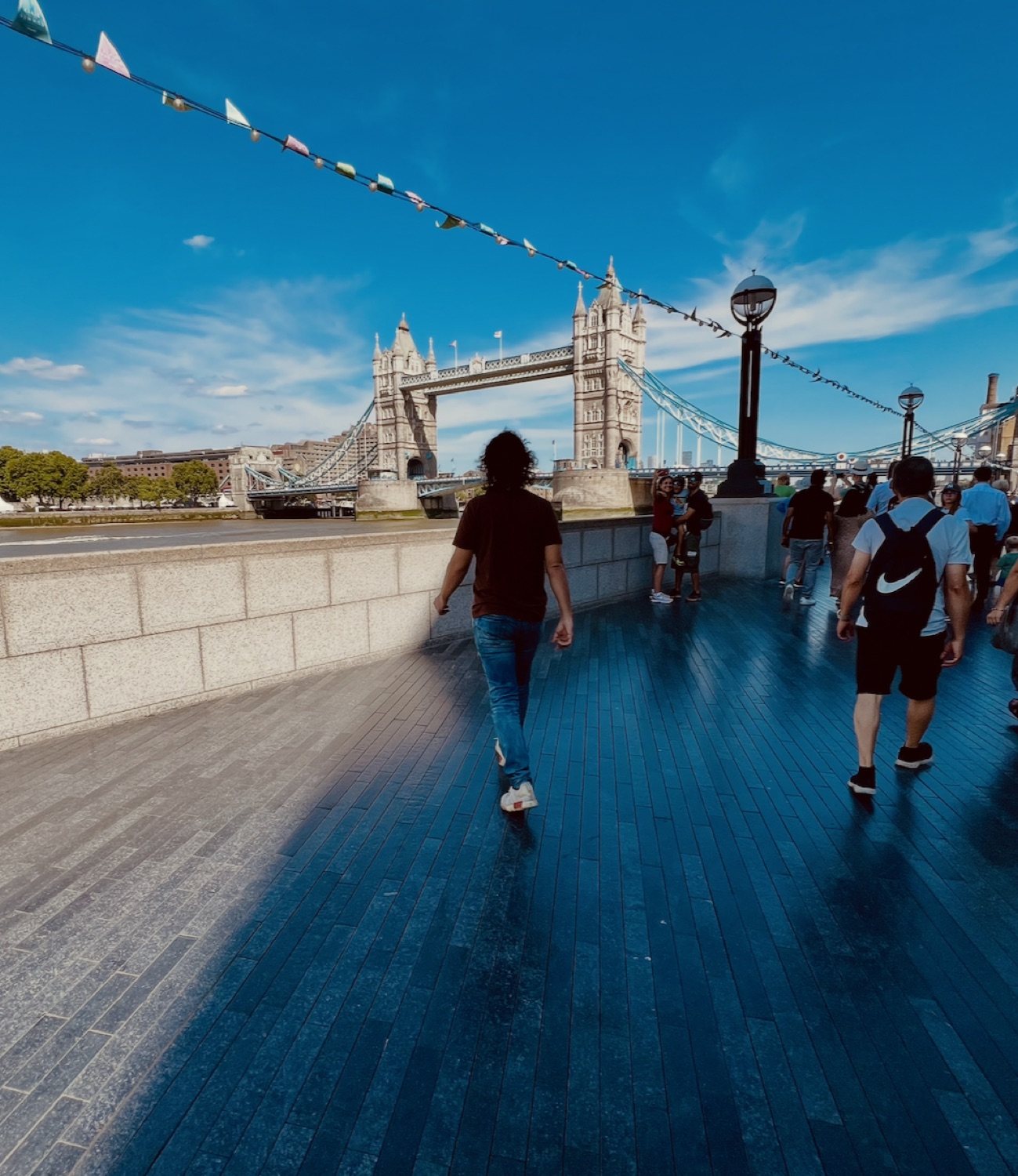 Tristan walking toward Tower Bridge in London, under a line of bunting, on a bright day